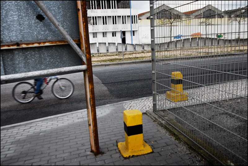 Ciclista numa rua industrial, com um poste amarelo e preto em primeiro plano